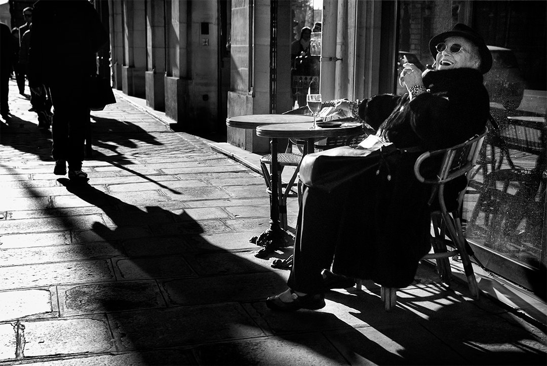 A person sitting at a pavement table among light and shadows.